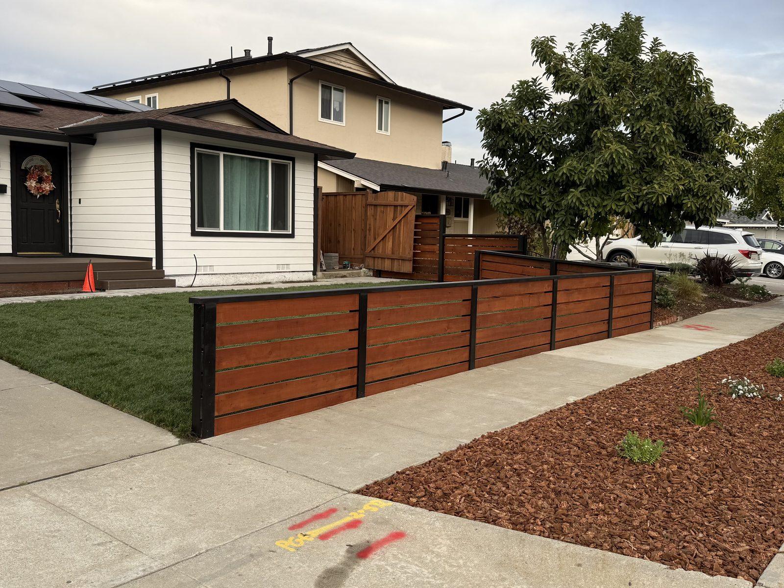 Completed horizontal redwood fence running the front boundary, with new lawn and a mulched planting bed behind it