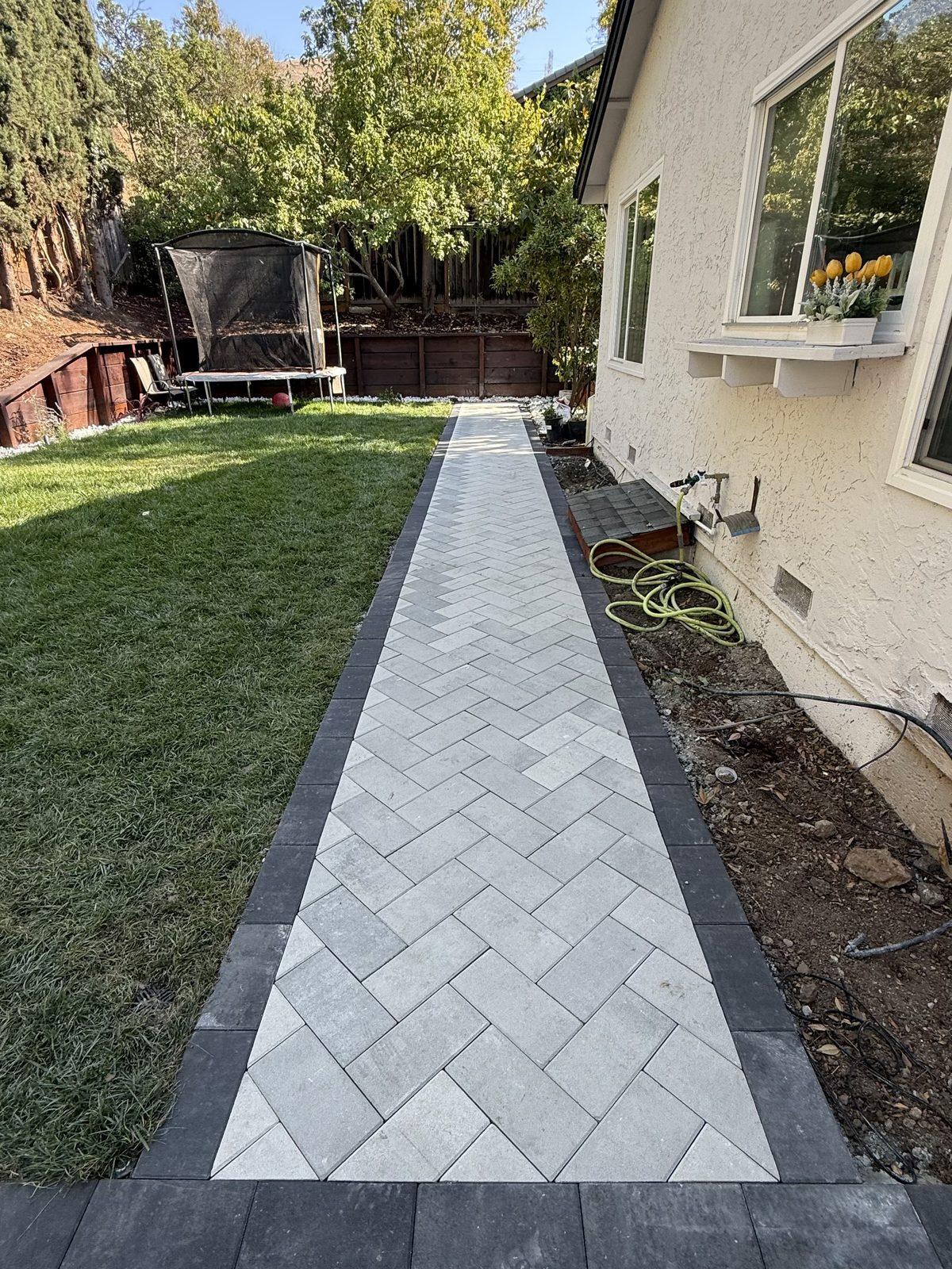 Paver walkway laid in a herringbone pattern with a contrasting double border, running between lawn and house