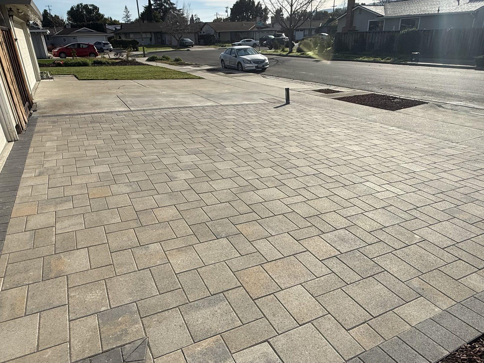 Finished interlocking paver driveway running the full width of a two-car garage, edged against the existing concrete apron