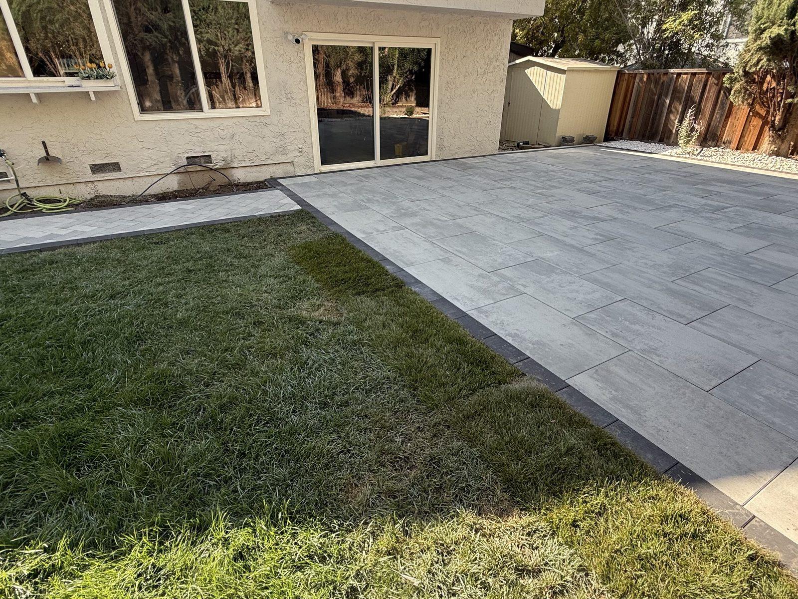 Finished large-format paver patio laid in a clean grid against the lawn, with a dark contrasting border