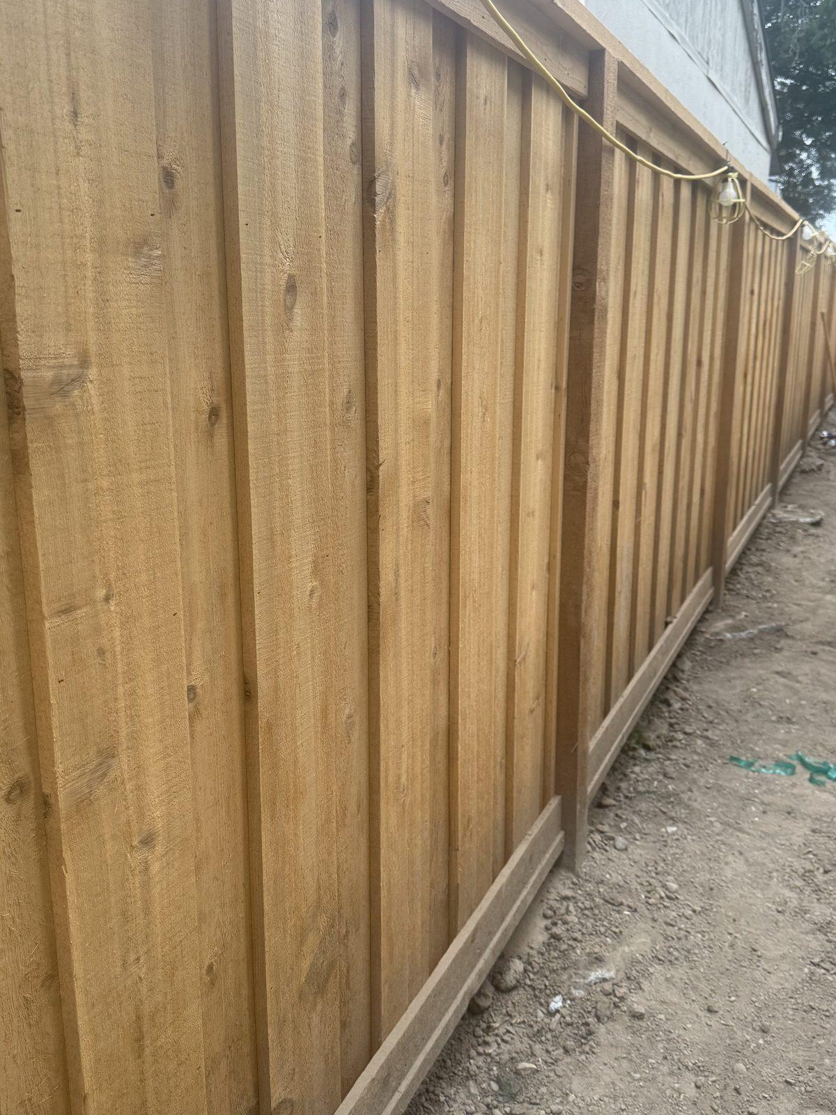 Newly built redwood board fence running the length of a side boundary, set on a gravel bed