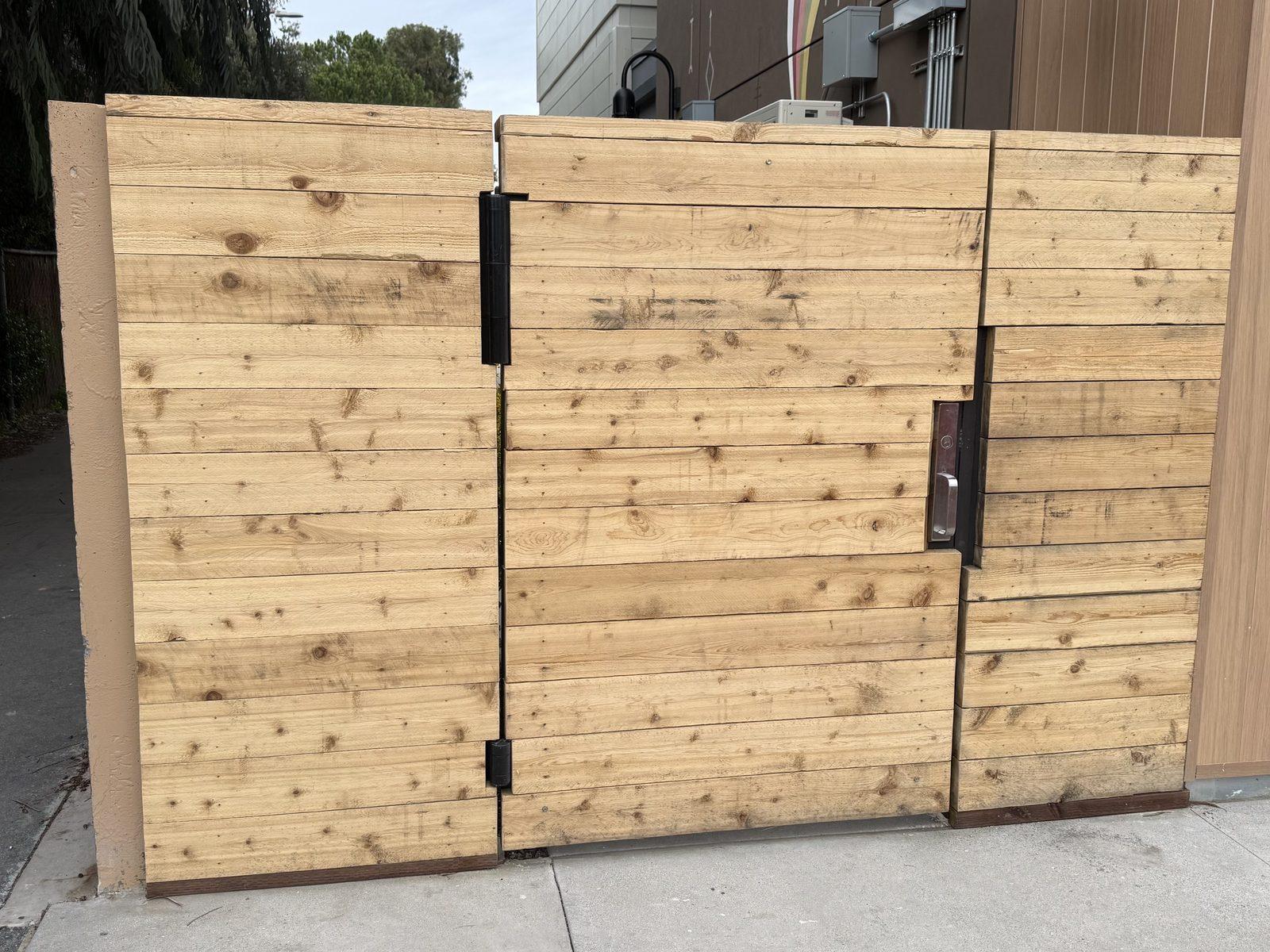 New double redwood gate with black hardware, hung between fence panels across a side access
