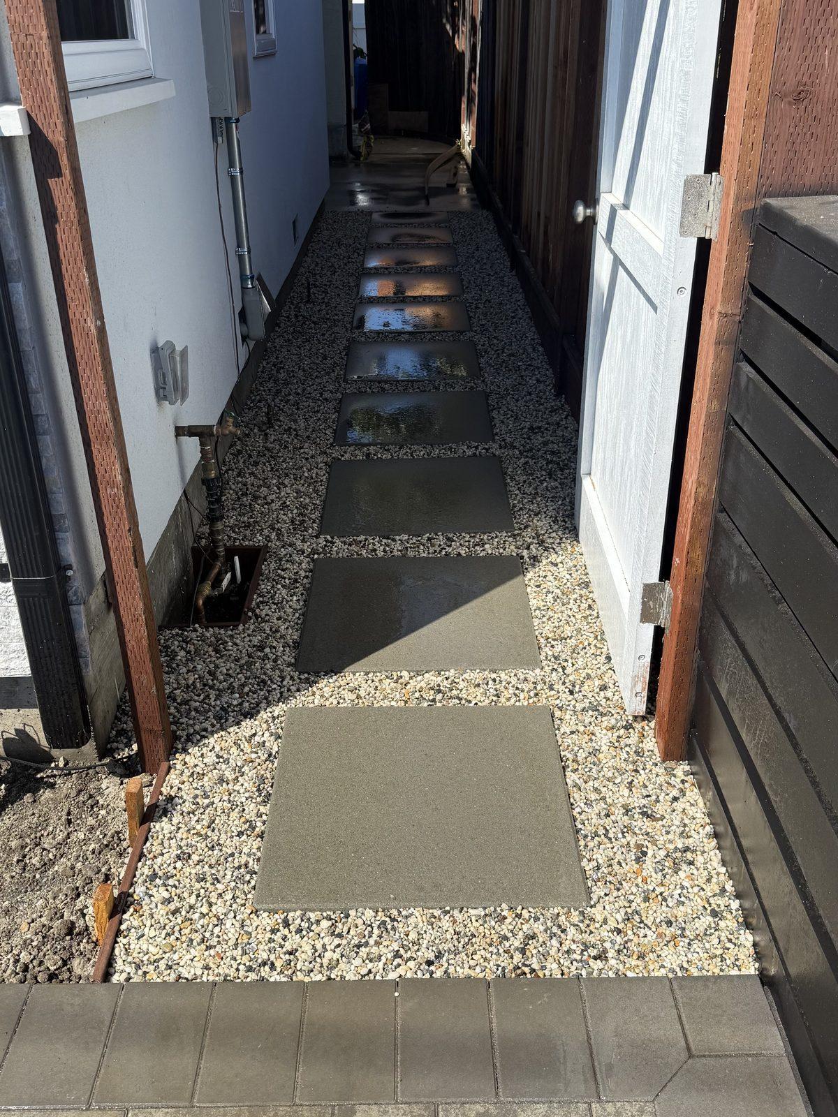 Narrow side yard finished with square concrete stepping pads set into gravel between the house and fence