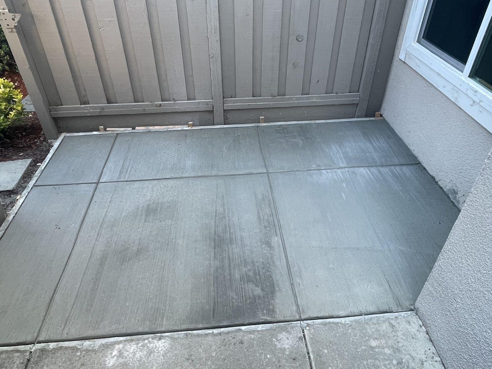 Finished concrete patio filling a narrow side yard, cleanly floated between the fence and the house wall