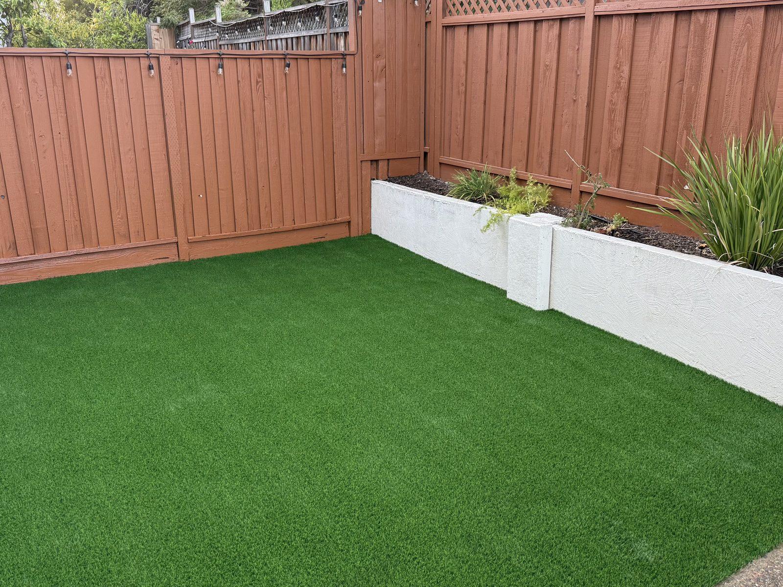 Finished artificial turf lawn filling a fenced courtyard, edged by rendered planter walls